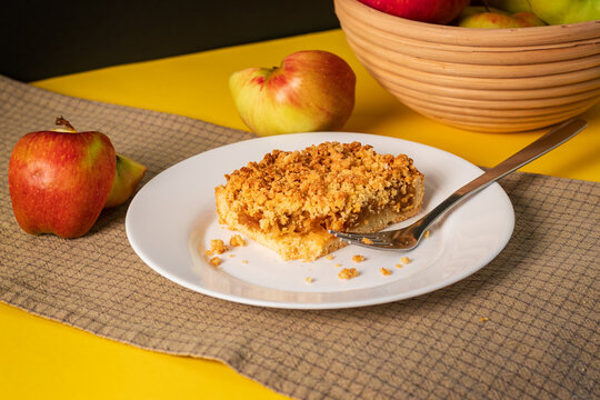 A slice of an apple pie on white plate against yellow background.  Tasting  an apple crumble pie. Autumn dessert. 