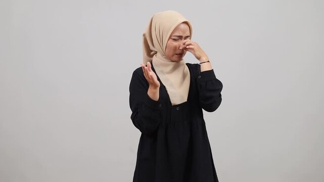 Bad smell. Young adult Asian muslim woman standing pinching her nose with fingers to hold breath, disgusted by stinky intolerable smell