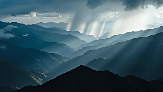 Multiple rainfall shafts descend beneath a dark thundercloud above layered blue mountain ranges, forming luminous vertical streaks across a vast remote valley filled with haze and atmospheric depth