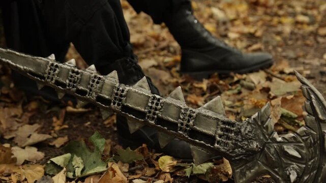 Weapon forest, Forest hammer, Weapon closeup. Spiked metal weapon is situated on fallen leaves within forest, with boots evident in background.