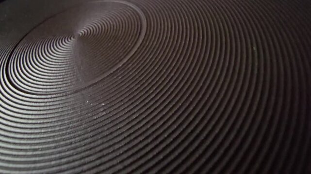 Detailed close-up of a dark circular spiral heating plate on an electric stove, highlighting industrial design, metallic ridges, and heat distribution surface.