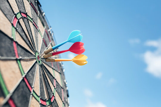 Dart in bullseye of dartboard with blue sky background  hitting target, goal and success