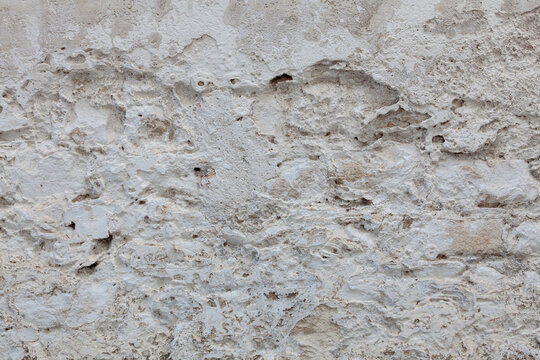 Rough plaster surface with flaking layers, micro-fractures, exposed mineral matrix, and heterogeneous surface morphology caused by long-term environmental degradation.