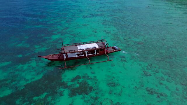 Traditional wooden boat with outriggers navigating clear turquoise waters at Turtle Beach. Concept of exclusive travel, vacation, and tropical adventure. Nice aerial view drone panorama shot from abo