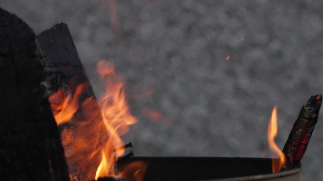 4k static close-up, burning wood with glowing embers, textured charcoal, and flickering flames creating a warm atmospheric fire scene in natural low light