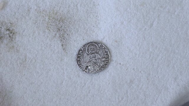 Close-up of a historic silver coin found beneath Shobak Castle, Jordan, showing a haloed figure, worn lettering and aged medieval-style minting on a white surface.