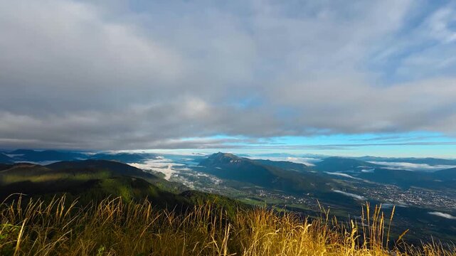 Sunrise timelapse from Trupejevo Poldne overlooking the valley near Villach, Austria, with low clouds drifting between alpine ridges beneath a changing morning sky.