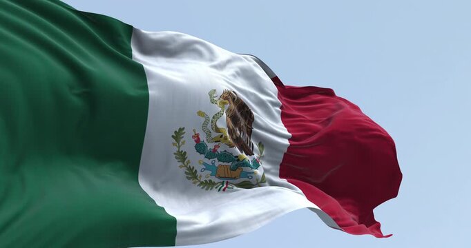 The Mexican flag with its coat of arms waving against a blue sky.