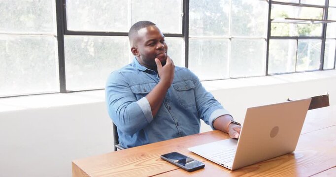 Using smartphone and laptop, African American man multitasking efficiently at office desk