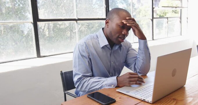 African American man in office looking frustrated while working on laptop