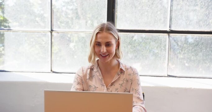 Businesswoman using smartphone voice assistant while working on laptop at office