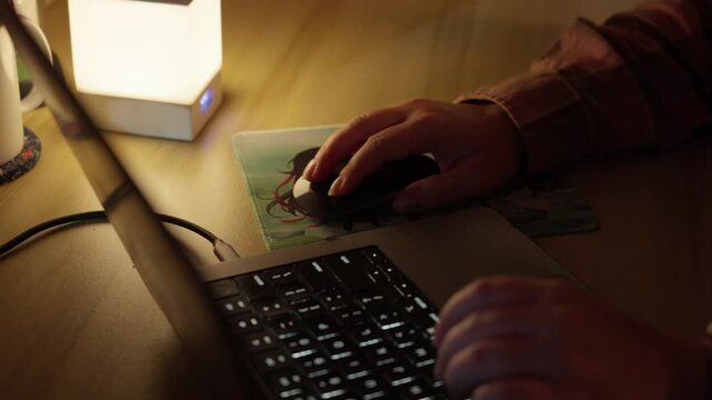 Hand Using Computer Mouse Beside Laptop in Warm Home Workspace