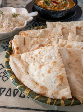 Fresh baked Indian naan flatbread slices served on a woven plate.