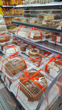 Various packaged cakes and pastries with red ribbons sitting on shelves in a grocery store or supermarket bakery section, offering a quick dessert or sweet snack option. Vertical photo
