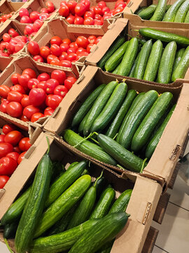 Cucumbers and tomatoes filling cardboard boxes at a grocery store, providing a vibrant display of fresh produce, highlighting healthy eating options and market shopping. Vertical photo