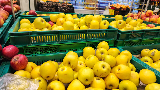 Golden delicious apples filling a large bin at a supermarket, with other fresh fruits and vegetables blurred in the background, promoting healthy eating and fresh produce.