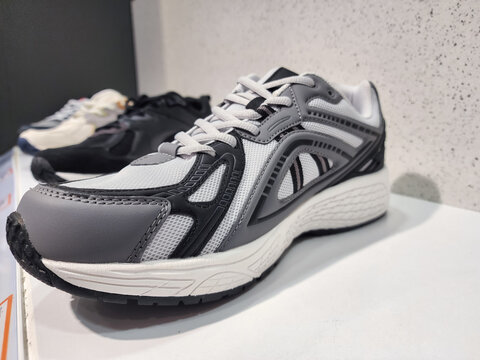 Row of various modern athletic shoes on a white display shelf, showcasing new fashion trends and sporty footwear in a retail environment