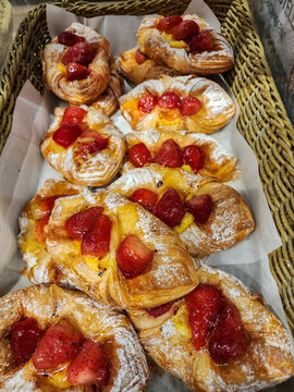Freshly baked strawberry custard danish pastries filling a wicker basket, dusted with powdered sugar, offering a delicious treat for breakfast or dessert. Vertical photo