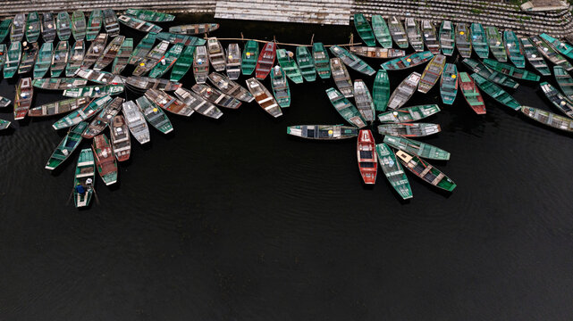 Colorful Boats on a Dark River. Aerial view of numerous traditional boats gathered on a dark river, creating an abstract pattern and striking texture on the water.