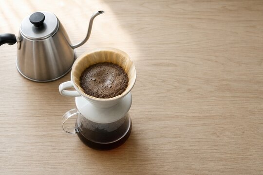 Pour over coffee maker with blooming grounds and a stainless steel gooseneck kettle preparing a fresh morning brew on a wooden table