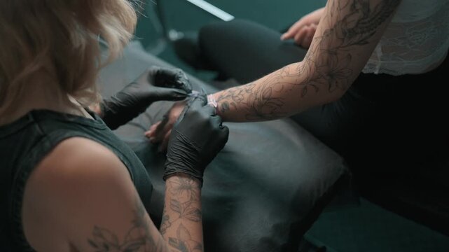 Tattoo artist prepares a clients forearm for a tattoo procedure, working with a stencil while wearing black protective gloves in a professional tattoo studio.