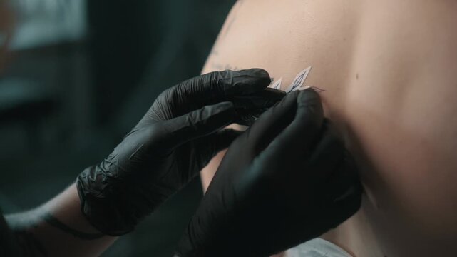 Tattoo artist carefully applies a floral stencil to a client's skin before tattooing, wearing black gloves in a professional tattoo studio.