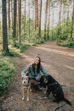 Active pet owner with two dogs in harnesses on a forest trail, illustrating responsible pet ownership, human-animal bond, outdoor recreation and companionship.