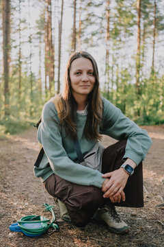 Female dog owner crouching on a forest trail beside leashes and outdoor gear, portraying daily pet care, dog walking lifestyle and active recreation in nature.
