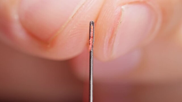 Red Thread Passes Through a Sewing Needle Eye on a Black Background, Detailed Macro View of Hand Sewing and Textile Craft Preparation