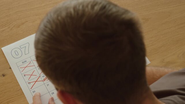 Person crosses off calendar days one by one while counting down to a marked birthday, representing anticipation, celebration and an upcoming special day.