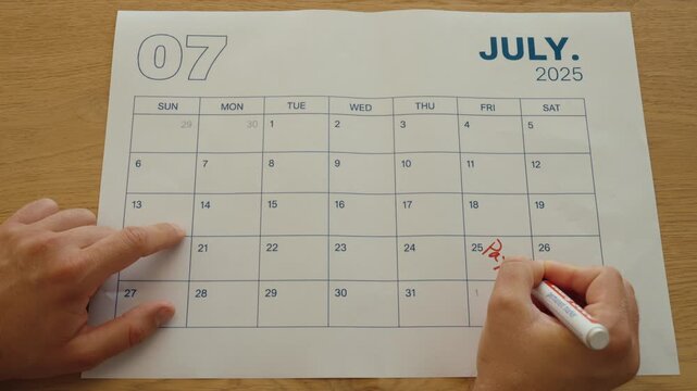 Close-up of a person writing &ldquo;Payday&rdquo; on a monthly calendar, marking the expected salary payment date and planning personal finances.