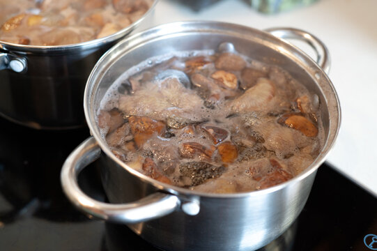 Mixed wild mushrooms boiling in a pot, including porcini, orange-capped boletes and slippery jacks. Mushroom cooking, seasonal harvest, homemade food and natural ingredients.