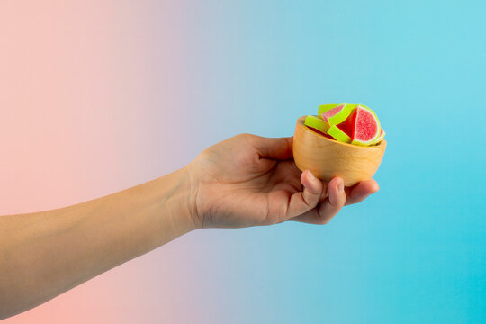 Sugar-coated jelly in a wooden cup, held in a hand against a colorful background.