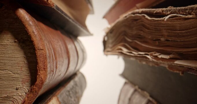 Cinematic slow push-in through stacks of old vintage books, filmed with a probe lens. Detailed close-up perspective of aged book spines and pages creates an atmospheric visual representing education
