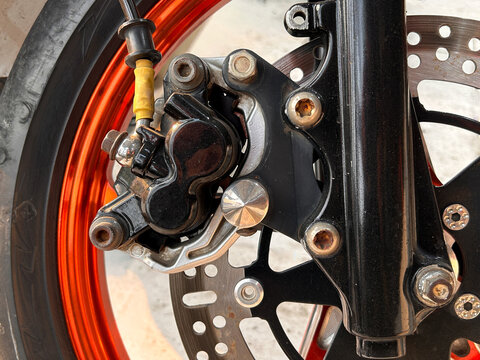 Detailed view of motorbike front suspension fork, caliper bracket, and anodized rim.
