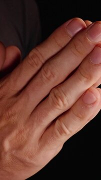 Vertical video. Adult Hands Pressed Together in Prayer Against a Dark Background, Expressing Faith, Reflection and Hope