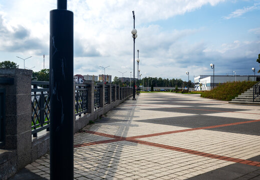 Wide paved public square with linear perspective of streetlights and metal fence under sky with copy space