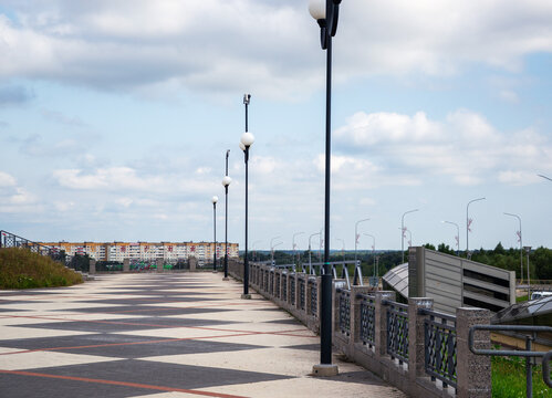 Row of modern tall streetlights along wide paved pedestrian overpass with geometric tile pattern under cloudy sky with copy space