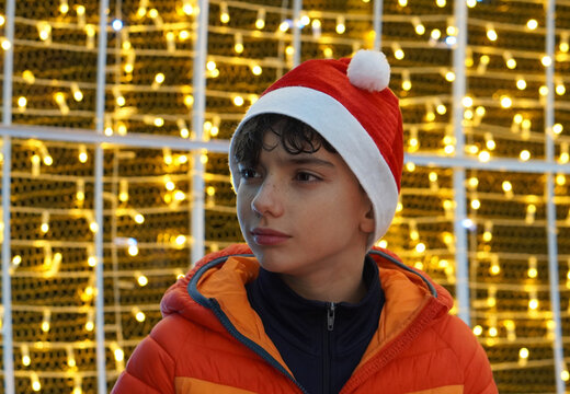 Portrait of a teenage boy wearing a Santa hat in front of some out-of-focus Christmas lights