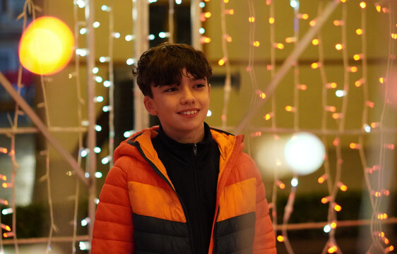 Portrait of a preteen boy in warm clothing standing in front of some out-of-focus Christmas lights in shades of gold
