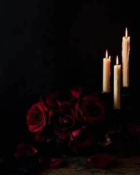 Dark red rose bouquet with three burning candles in a low key Gothic setting, romantic Halloween background with large black copy space for text, invitations and banners