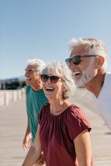 Fototapeta premium Three happy seniors laughing on boardwalk background for retirement lifestyle banner and travel poster