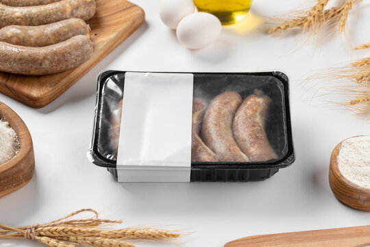 Raw kupati sausages packed in plastic container with blank label mockup surrounded by flour top view