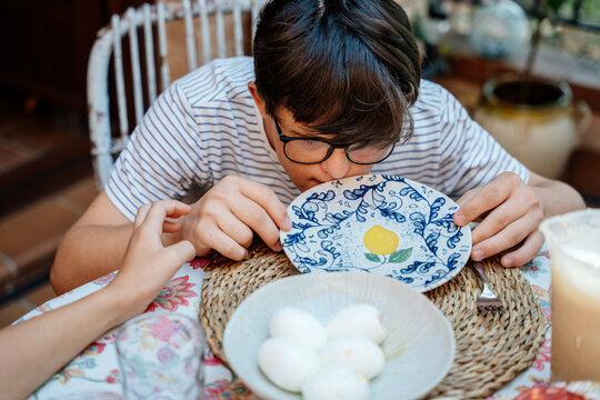 Teenage boy with Down syndrome finishing breakfast during everyday family life at home in Spain