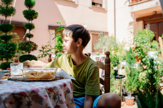 Young boy sitting at outdoor breakfast table in sunny family courtyard in Spain