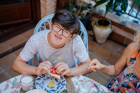 Teenage boy with Down syndrome enjoying breakfast sandwich during everyday family life in Spain