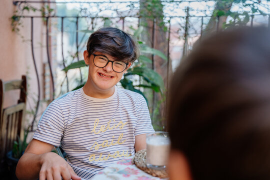 Smiling teenage boy with Down syndrome relaxing after breakfast with family at home in Spain