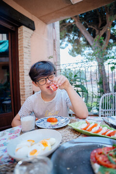 Vertical portrait of teenage boy with Down syndrome enjoying tomato sandwich during breakfast in Spain