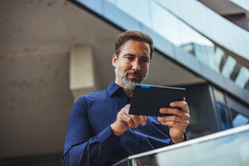 Businessman Using Tablet Outside Modern Office Building, Confident Middle-Aged Professional © Dragana Gordic