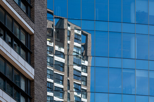 Modern blue glass facade in London England shows reflection of an older building creating contrast in architecture within a layered urban city composition